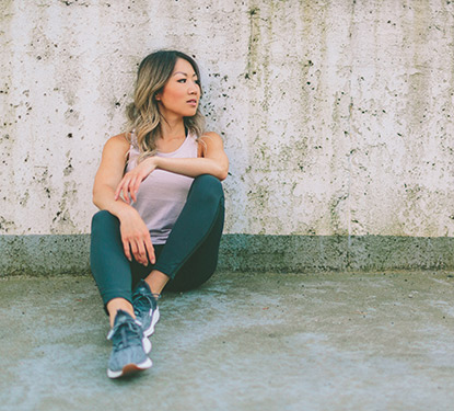A young woman wearing athleisure wear sitting against a concrete wall