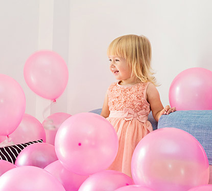 A young girl in a pink dress surrounded by pink balloons