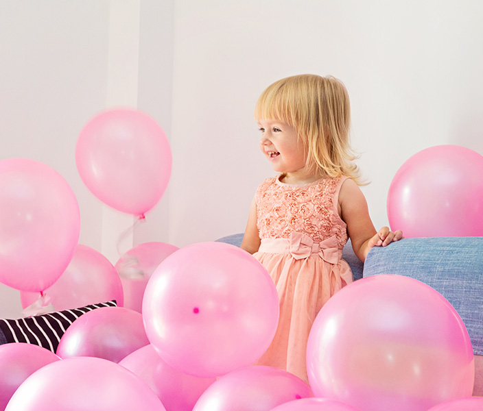 A young girl in a pink dress surrounded by pink balloons