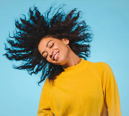Smiling woman in a yellow sweater tossing her hair