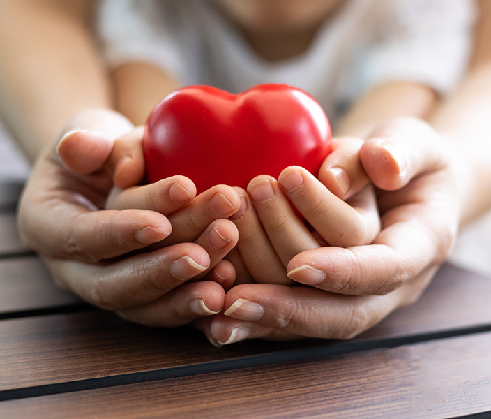 Parent and child's hands cradling a red heart-shaped toy