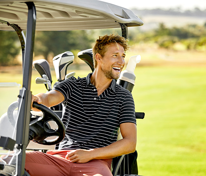 A man in stylish golf attire driving a golf cart