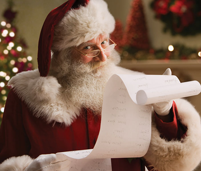Santa Claus reviews a long list in a warmly lit holiday setting.