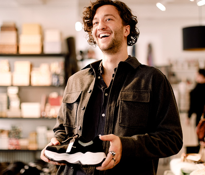 A young man holding up a sneaker in a store