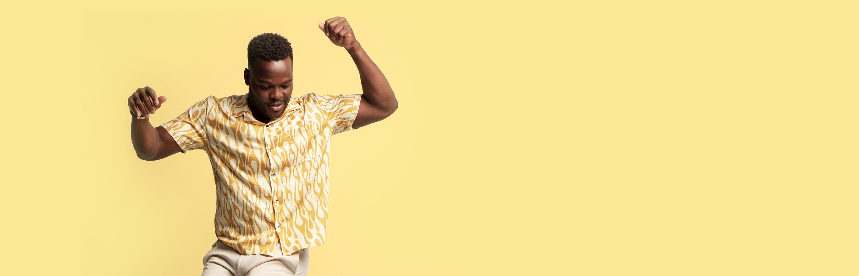 A young man striking a pose in a short-sleeve yellow and white shirt printed with a flame pattern
