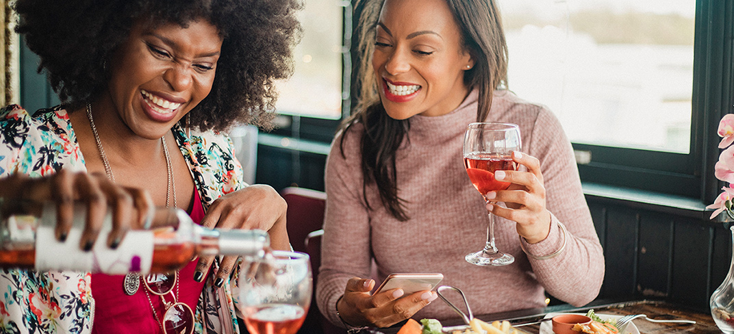 Two happy women enjoying a get-together with glasses of rosé at a restaurant