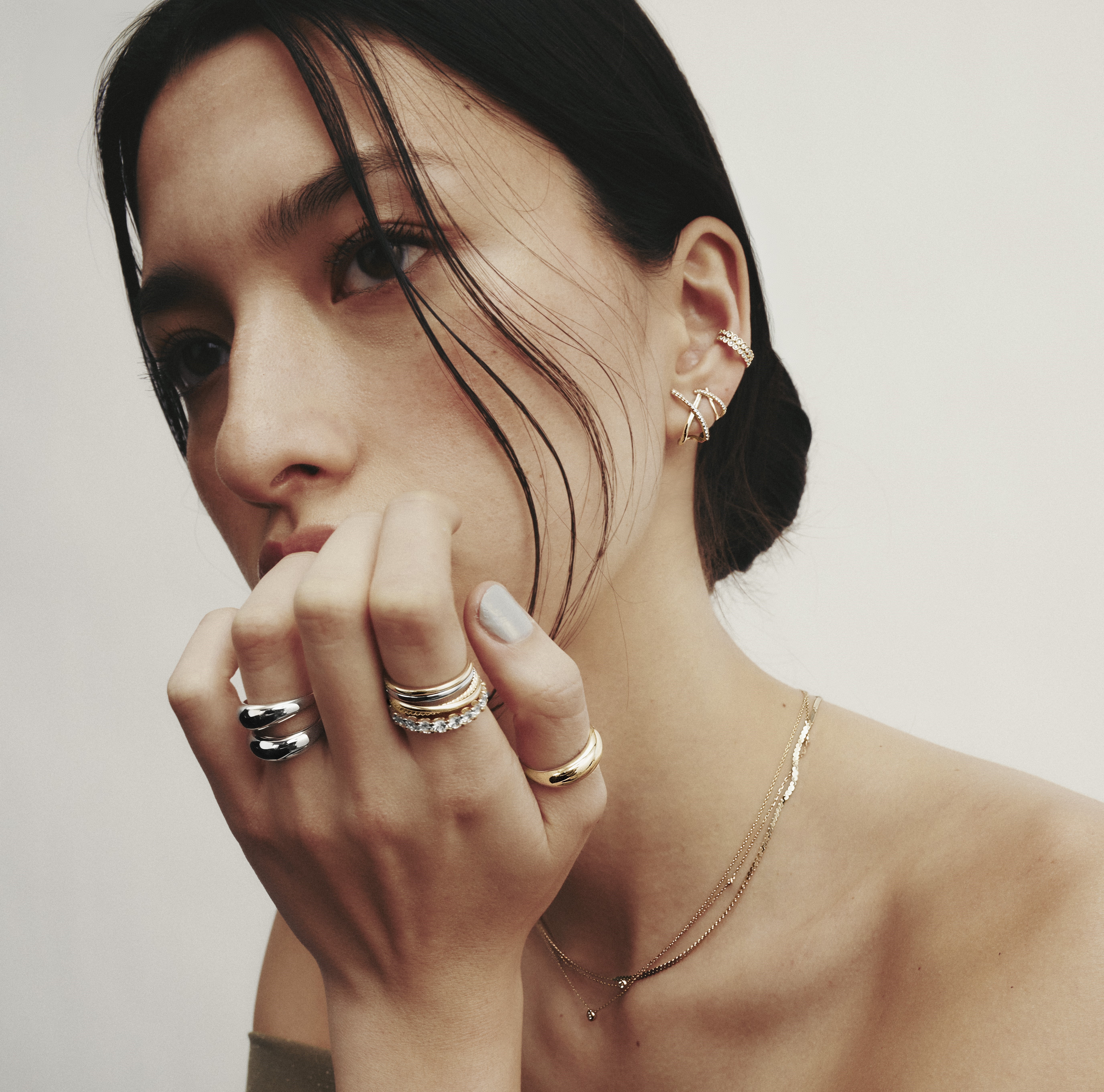 A dark haired woman wearing necklaces, rings and earrings from Mejuri