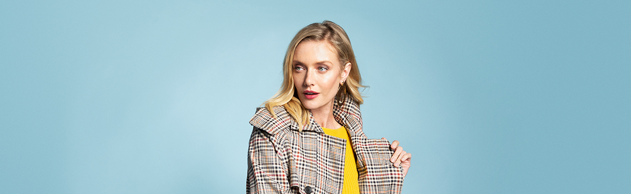 Blonde woman wearing a yellow sweater and plaid trench coat