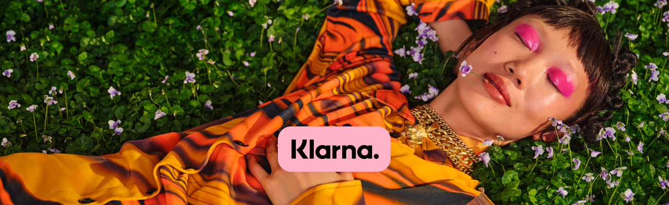 A hip young woman laying in a field, with the Klarna logo applied in the corner