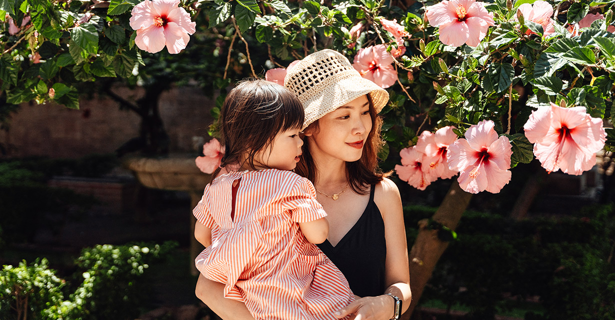 A mom holding her young daughter in front of flowers