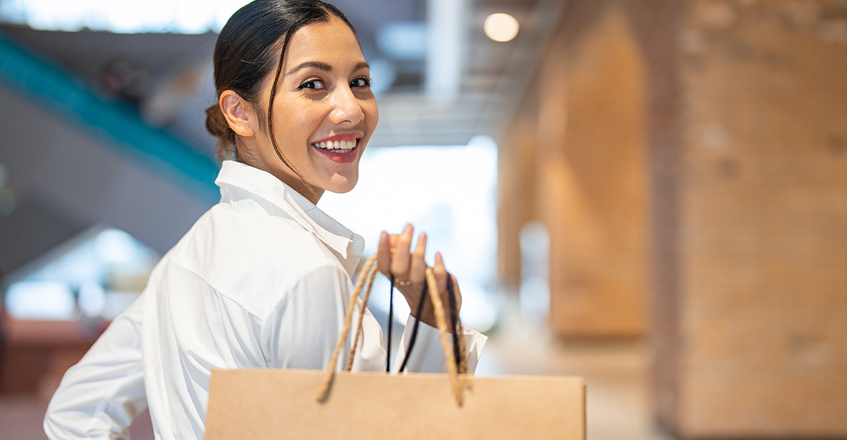 A smiling woman holding shopping bags over her shoulder