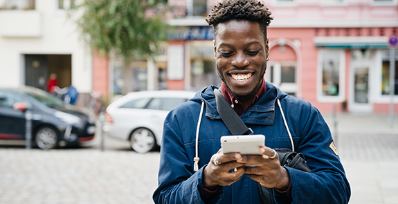 A smiling man texting on a sidewalk