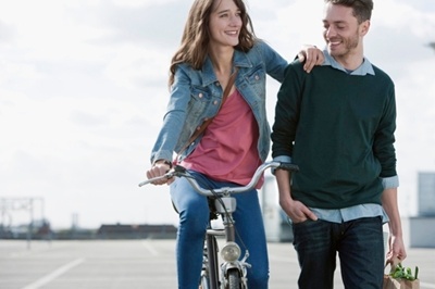 girl on a bike holding on to the shoulder of a guy and both are smiling.