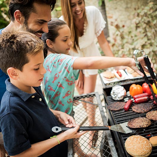 Father overseeing his family of 4 at the BBQ grill cooking food.