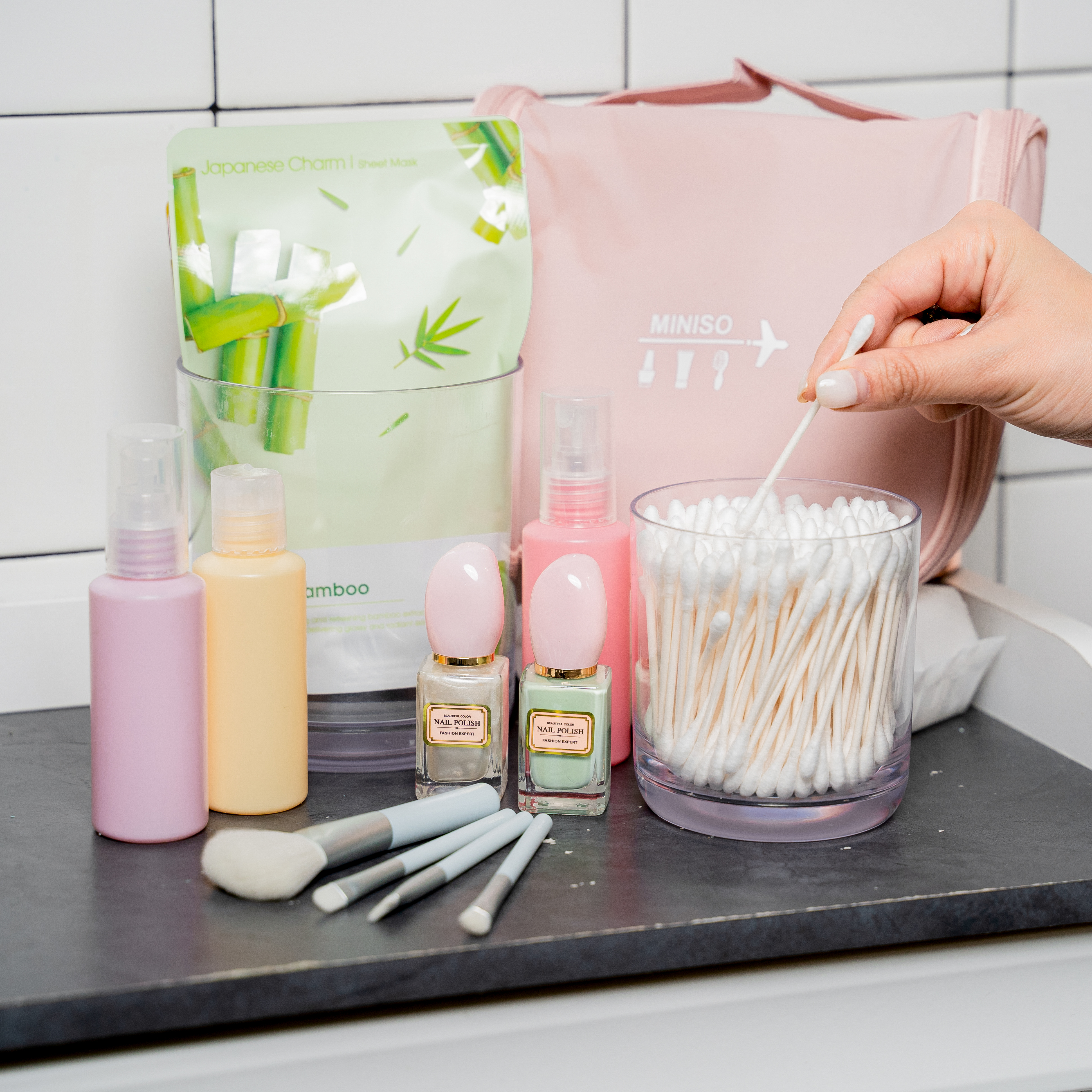 Various bottles of skin care product, cosmetic brushes, creams and q-tips on a black counter top.