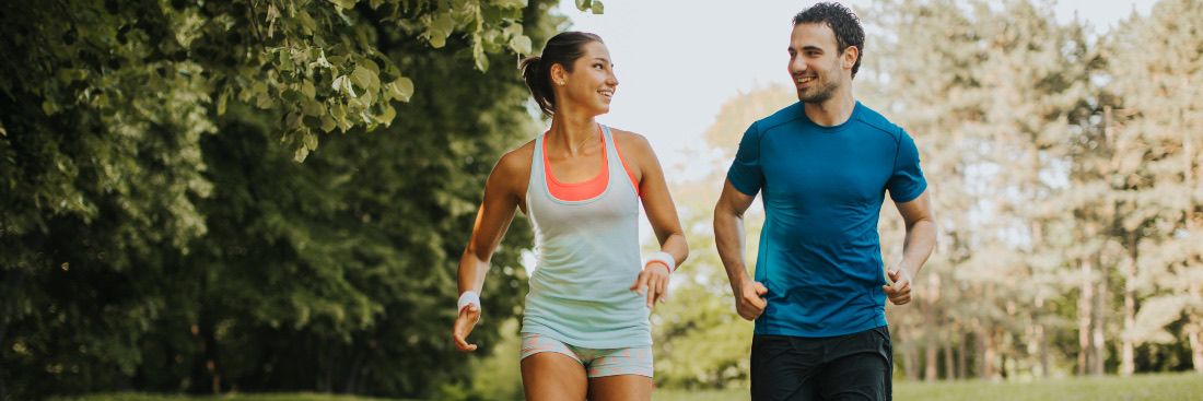 Sweaty woman and man exercising out in nature smiling at each other