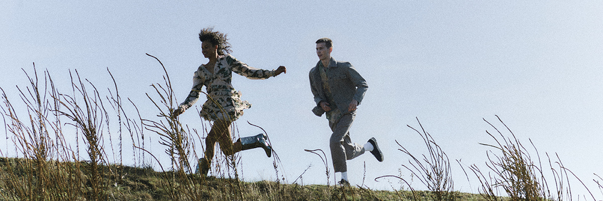 Young woman and man wearing AllSaints fashions and running in a field