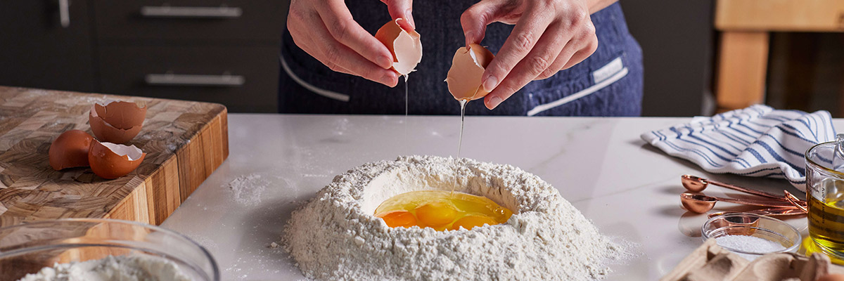 A cook making pasta by cracking eggs into flour